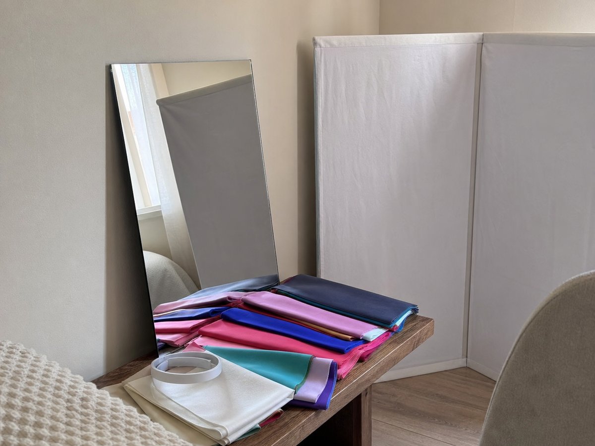 Colour analysis consultation space with a full-length mirror, two neutral beige panels and a stack of draping fabrics on a shelf