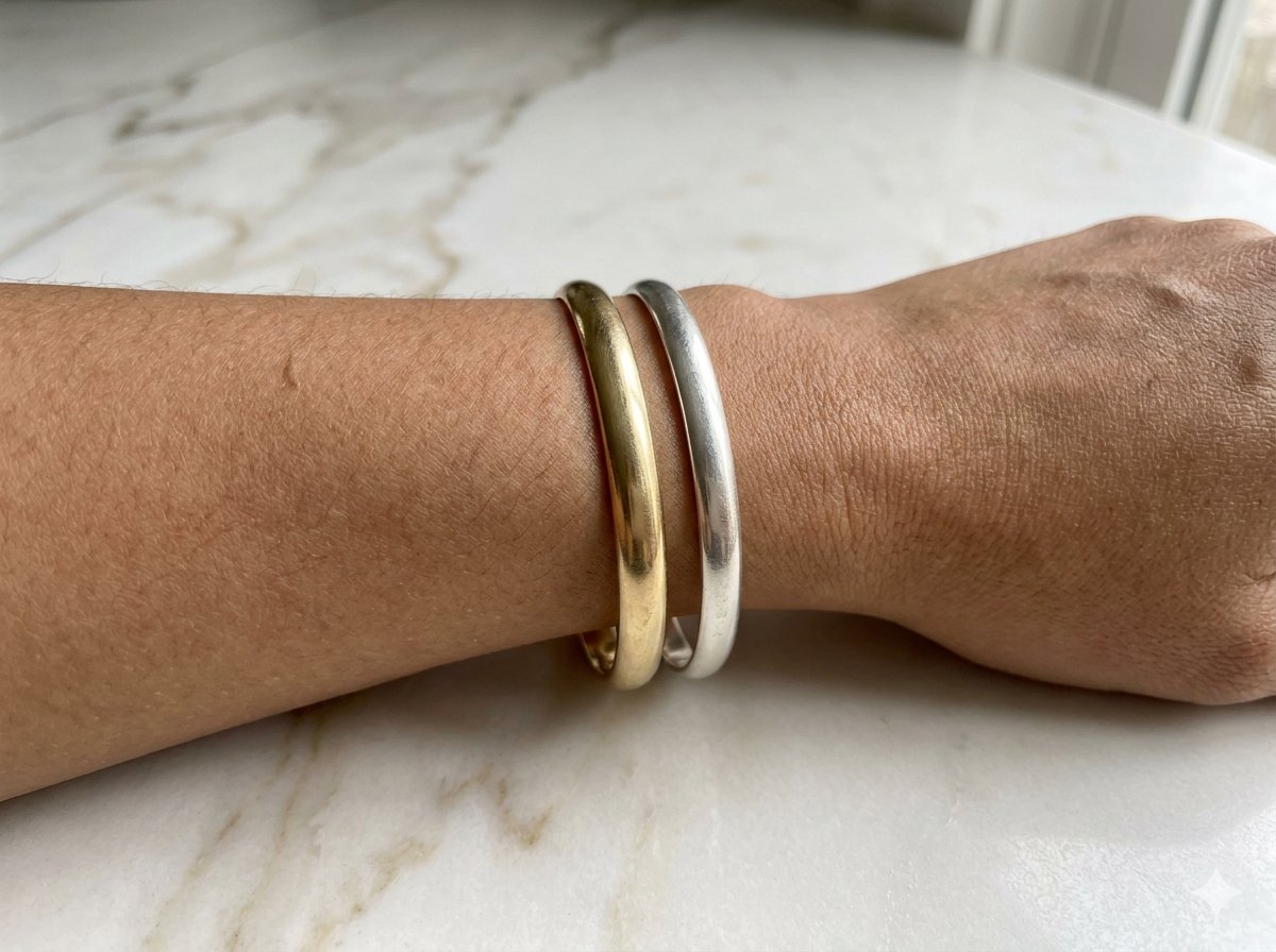 Wrist wearing a gold bangle and a silver bangle side by side to compare their effect on skin tone